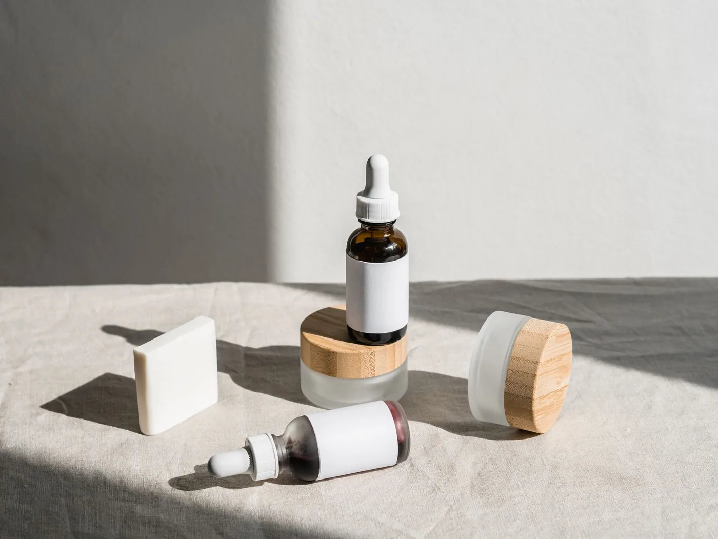 Minimal skincare bottles and jar on neutral surface, layering routine still life.