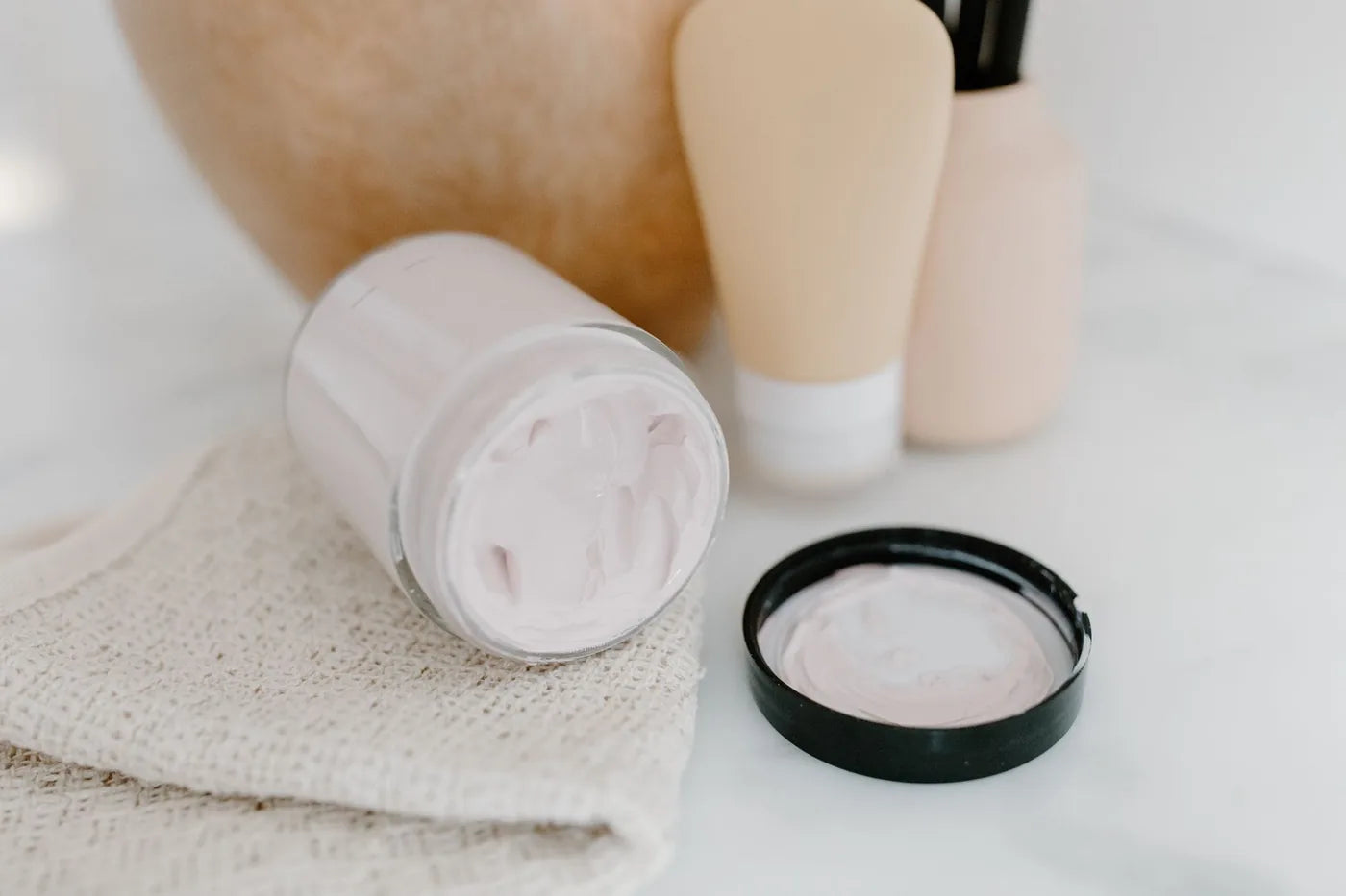 Clear glass jar in soft neutral light, minimal skincare formulation still life.