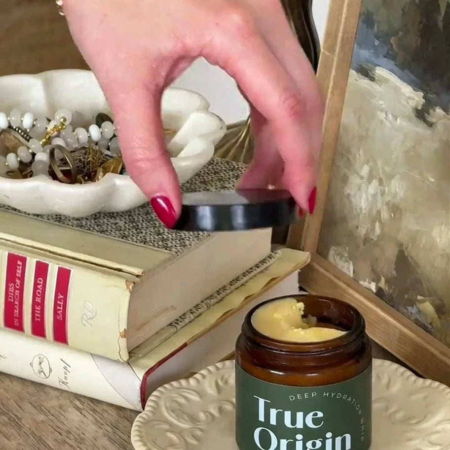 Hand lifting the lid off a Deep Hydration Whip jar on a styled vanity with books