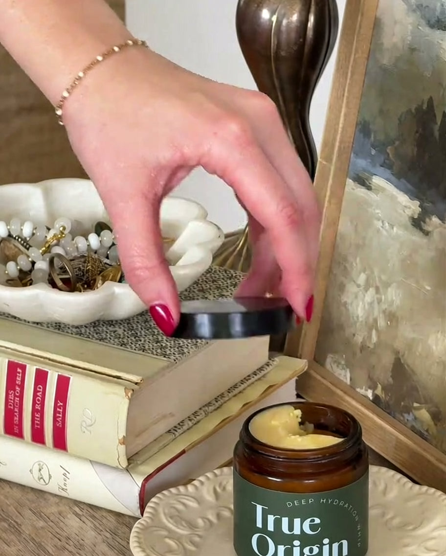 Hand lifting the lid off a Deep Hydration Whip jar on a styled vanity with books