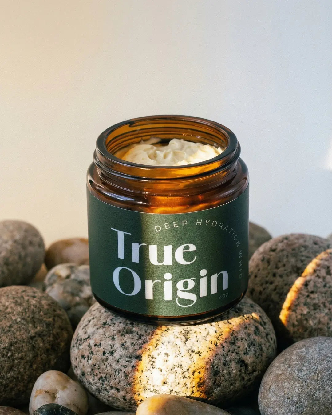 True Origin Deep Hydration Whip jar on river stones